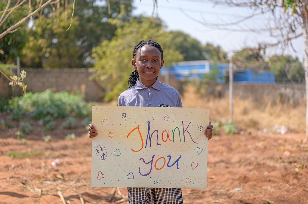 A young girl holding a handmade 'Thank You' sign