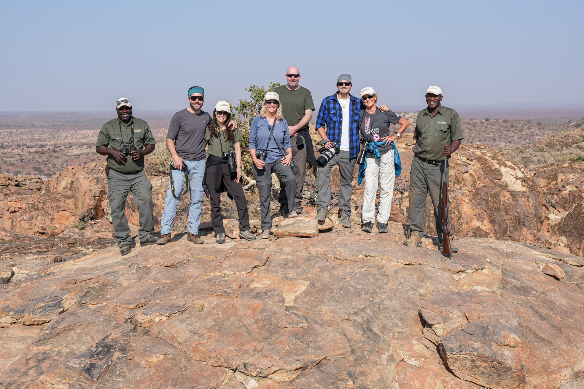 group of safari adventurers posing on a rocky hilltop with binoculars and cameras,