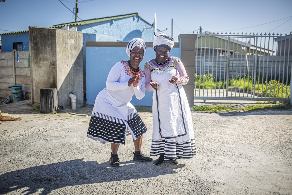 Two women in traditional white dresses pose and smile outdoors