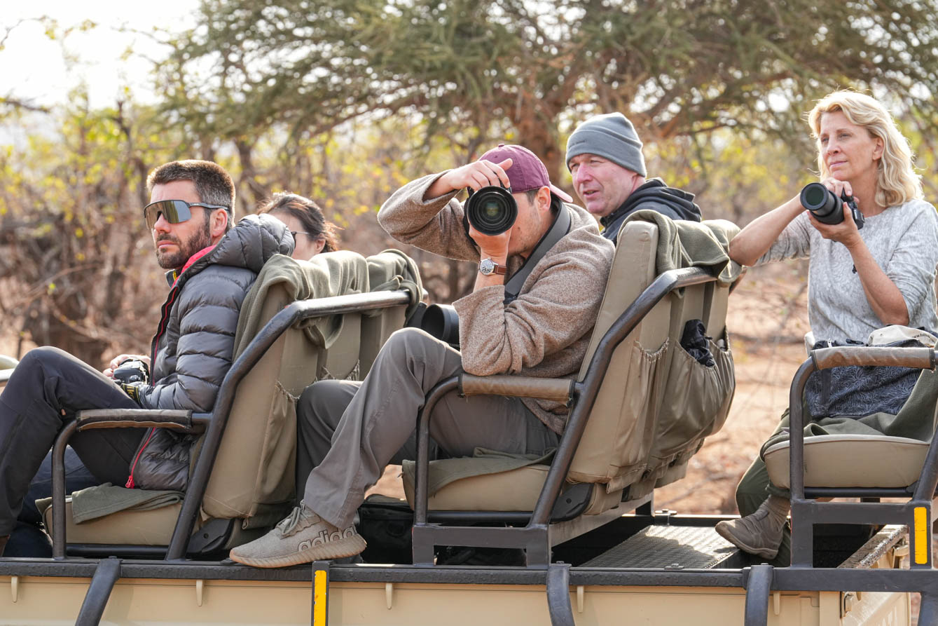 A group of people sitting in an open safari vehicle, holding cameras and observing their surroundings