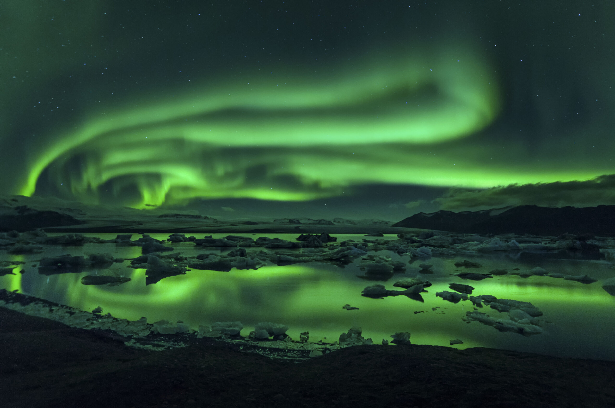 Green northern lights reflecting on icy waters at night