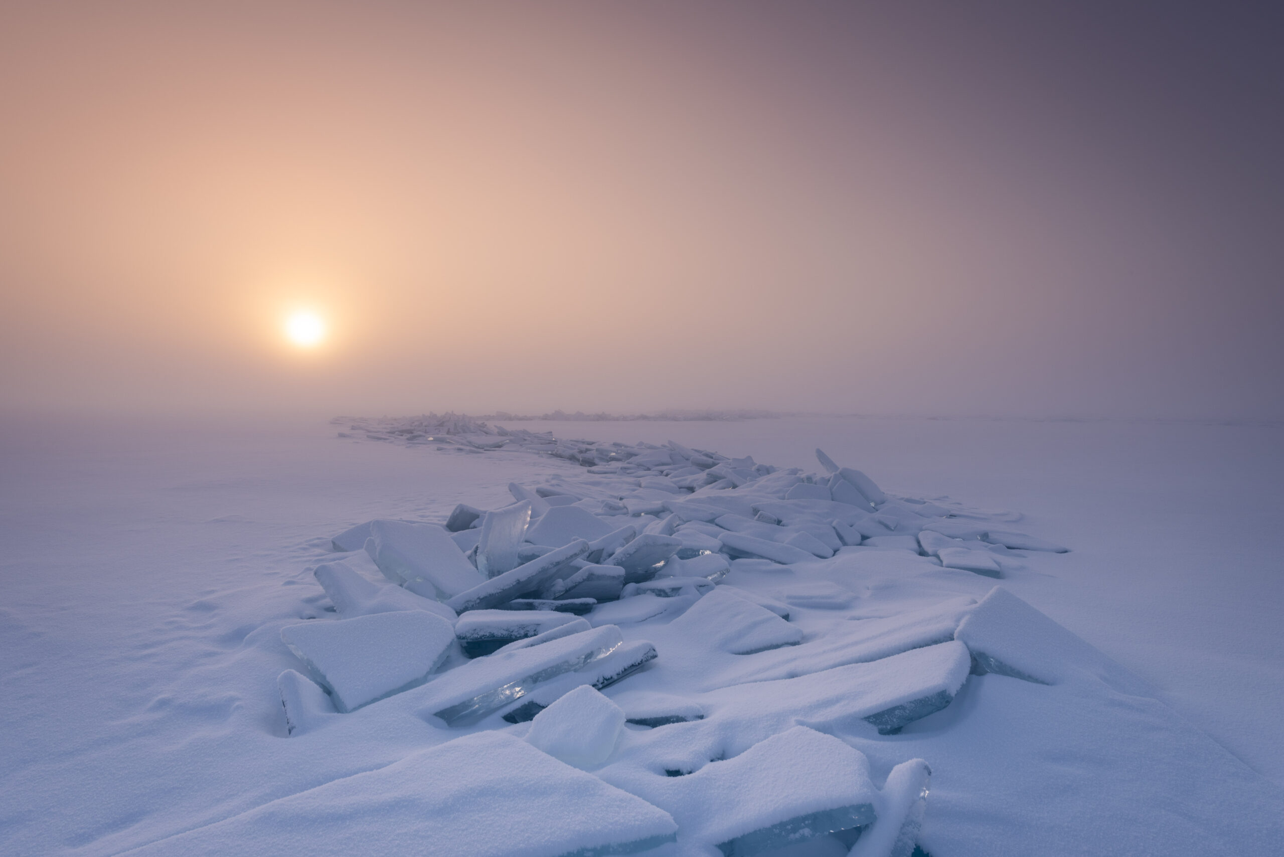 Sunset over a snowy landscape with broken ice slabs scattered on the ground