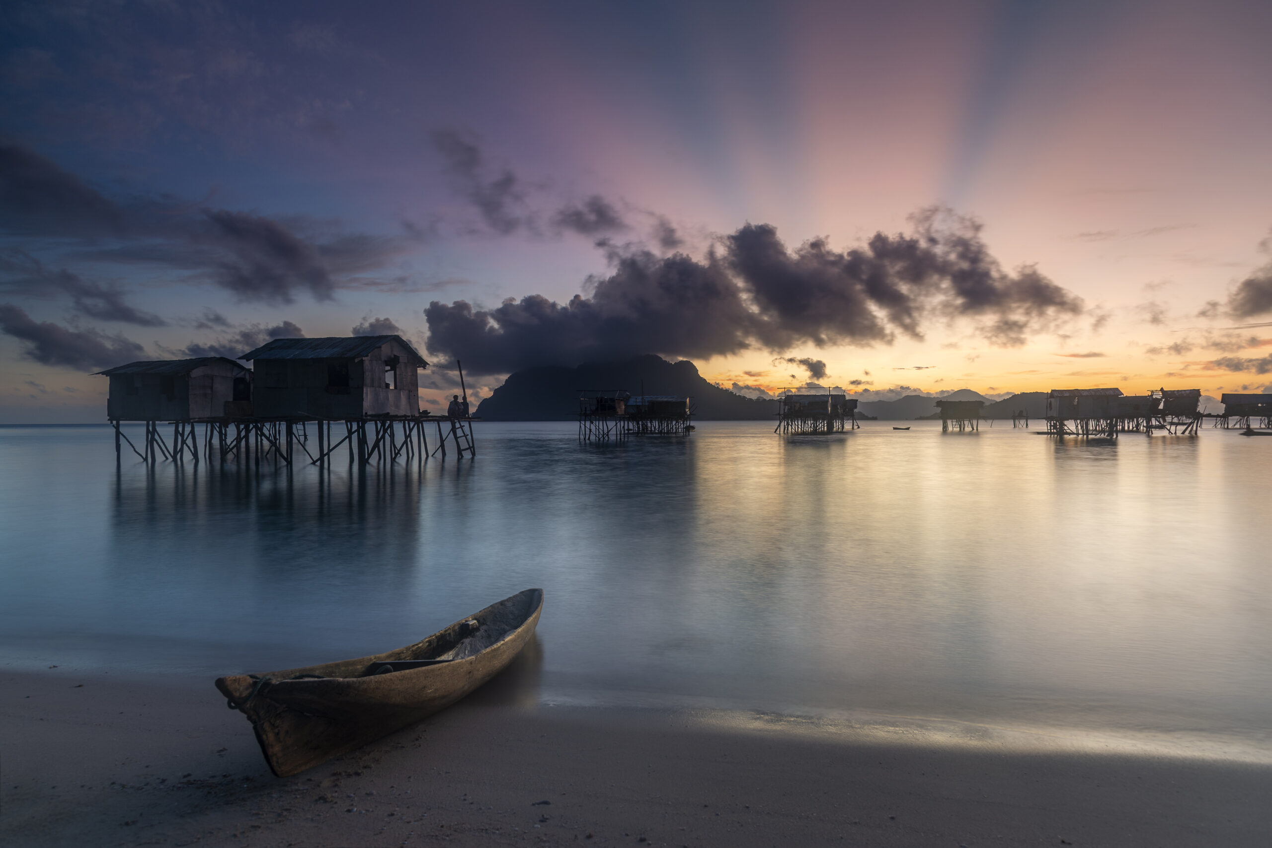 Stilt houses over the water at sunrise with a wooden boat on the shore