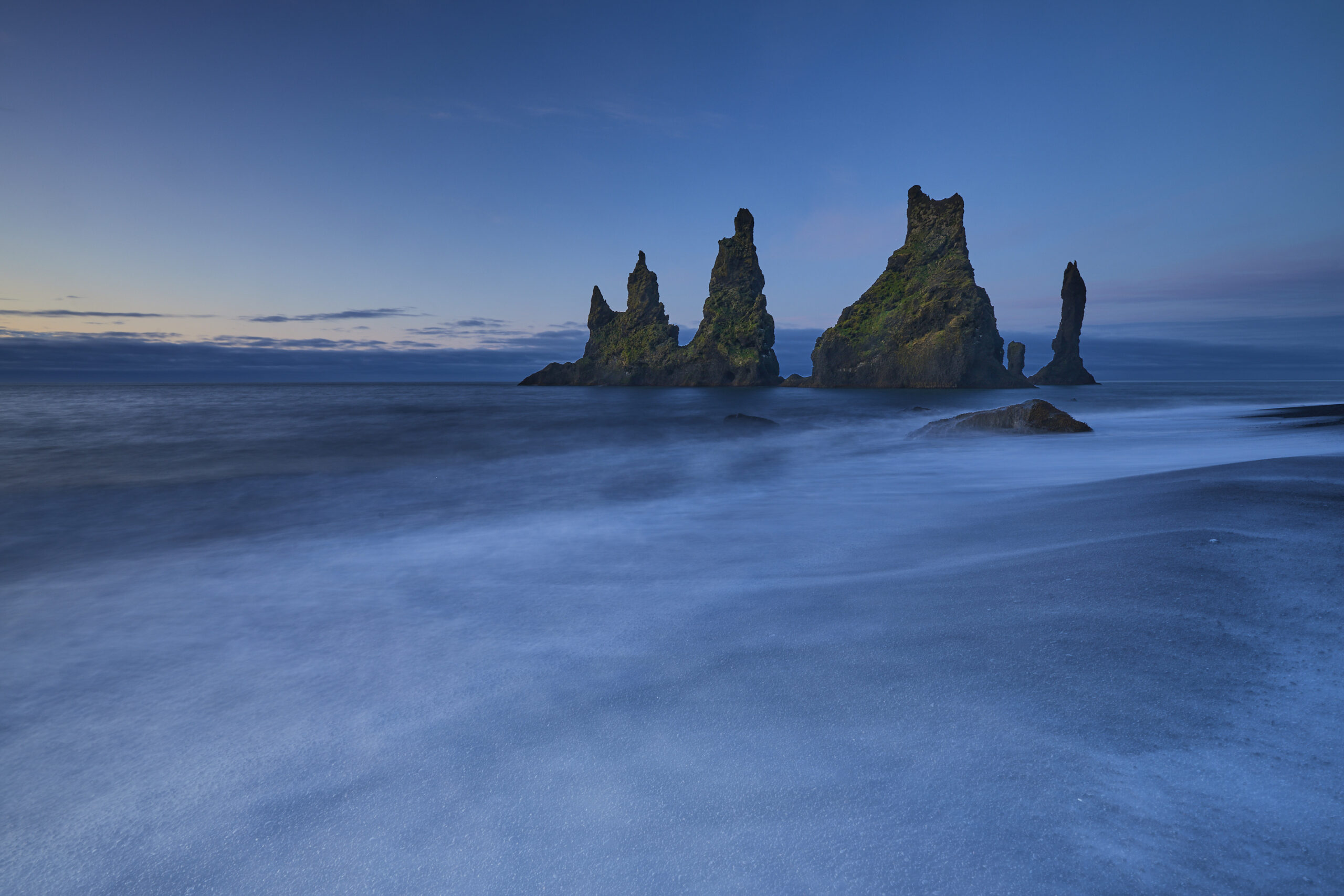 Tall rocky sea stacks rising from the ocean near a black sand beach