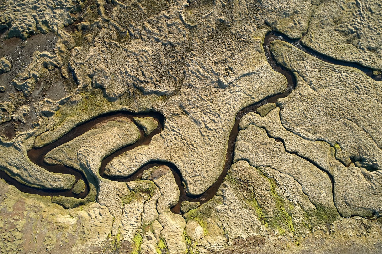 aerial view of a winding river cutting through a dry, textured landscape with patches of green vegetation