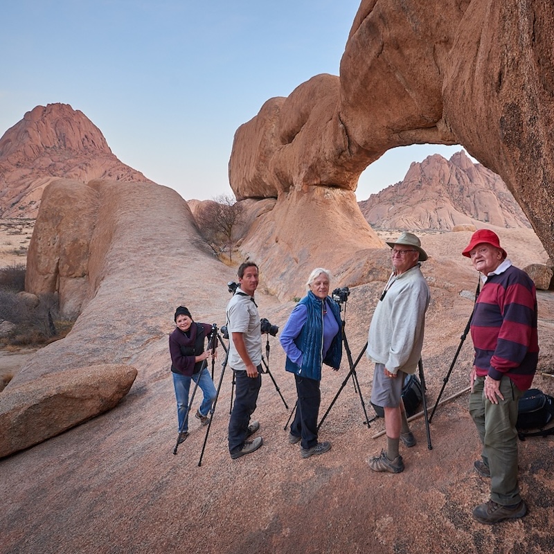 Group of photographers standing on rocks with tripods near a stone arch