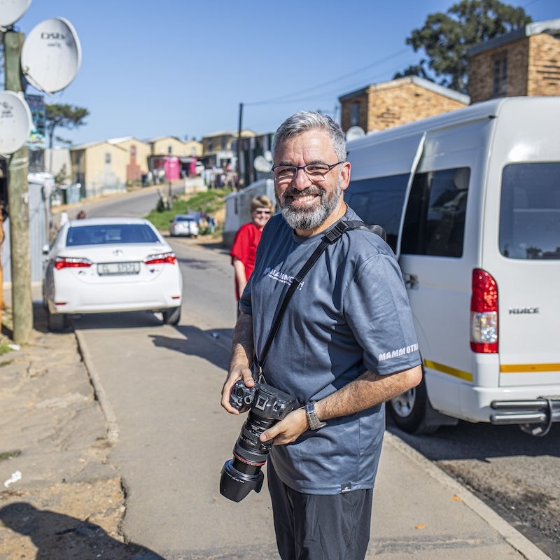 Man smiling with a camera on a sunny street