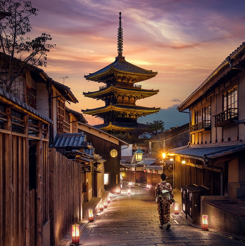 A person in traditional dress walks a lantern-lit street toward the iconic Yasaka Pagoda glowing under a pastel Kyoto sunset, captured during the Japan Photo Tour with Penda Photo Tours.